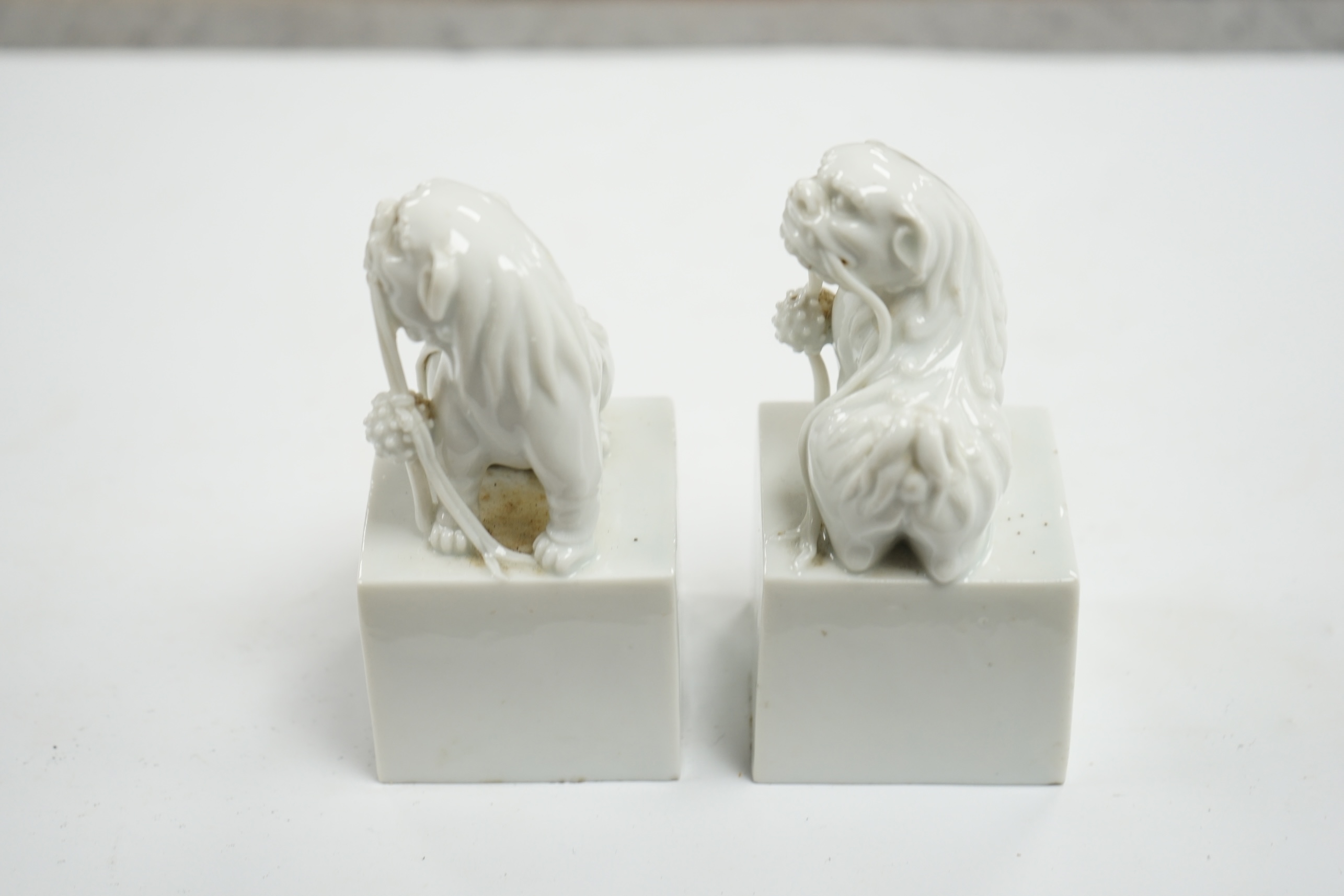 A pair of Japanese Hirado style white glazed porcelain Shishi lion-dog seals and a wooden stand, 10.5cm high. Condition - slight manufacturing glazing losses to base edges